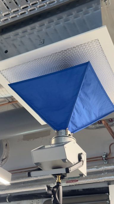 Blaues, konisches Tuch hängt unter einem Belüftungsgitter in einem Raum.